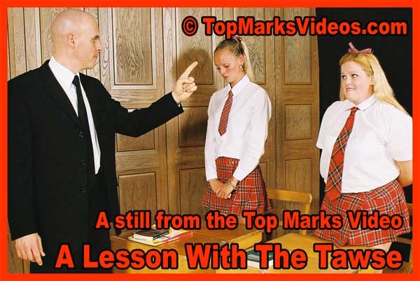 Strict male teacher Master Kain scolding and pointing at submissive blonde schoolgirls Lucy McClean and Monica in uniform during a tense school discipline scene, with another schoolgirl watching. Classic British corporal punishment setup from 'A Lesson With The Tawse' featuring hand tawsing preparation